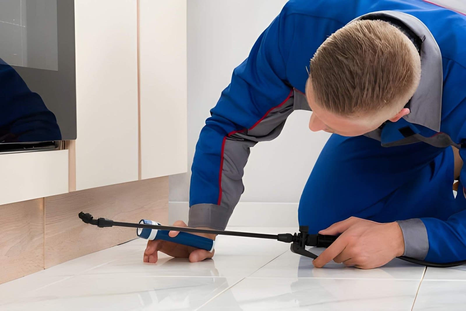Pest control Hobe Sound FL—technician spraying treatment near cabinet base during indoor inspection.
