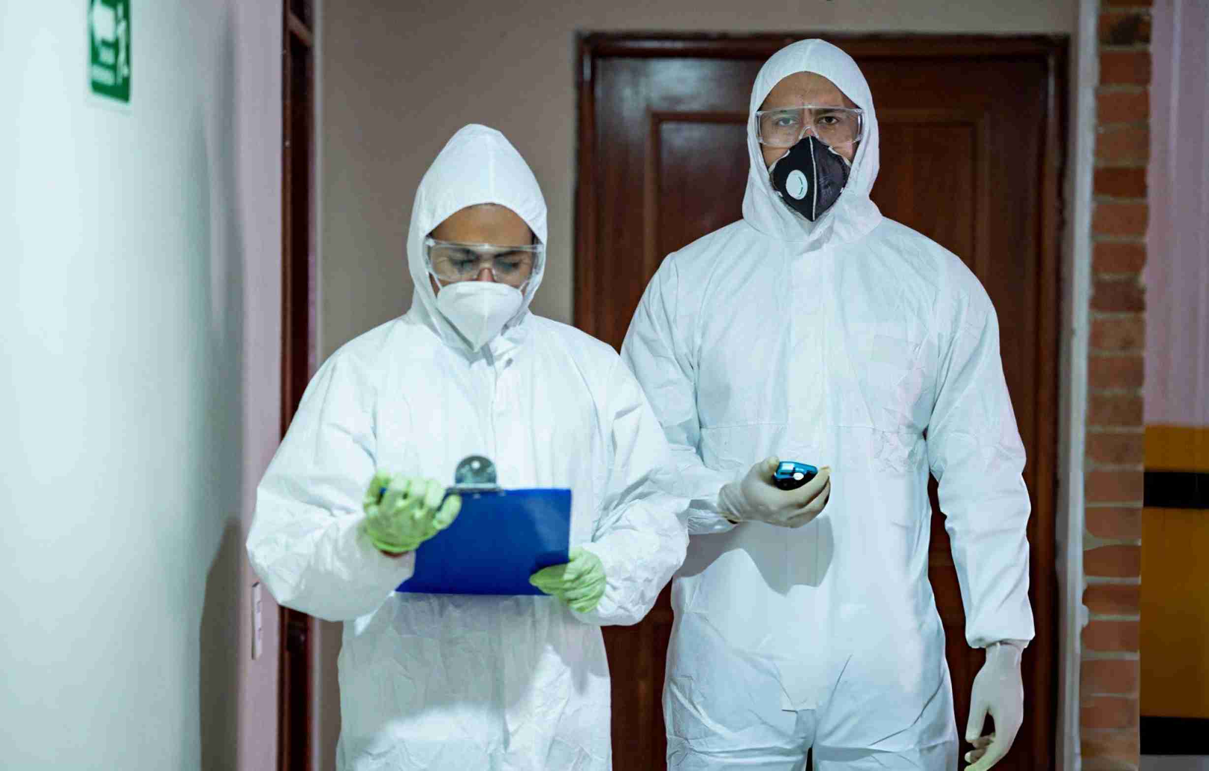 Pest control Hobe Sound FL technicians in protective suits conducting hallway inspection with clipboard and scanner.